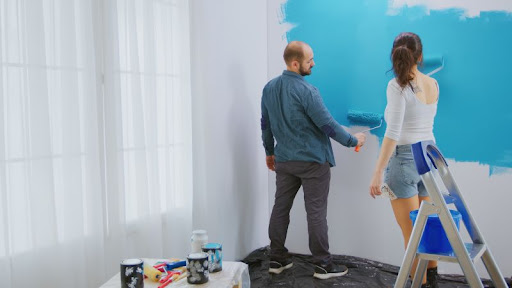mladý pár maľuje stenu v izbe na modro